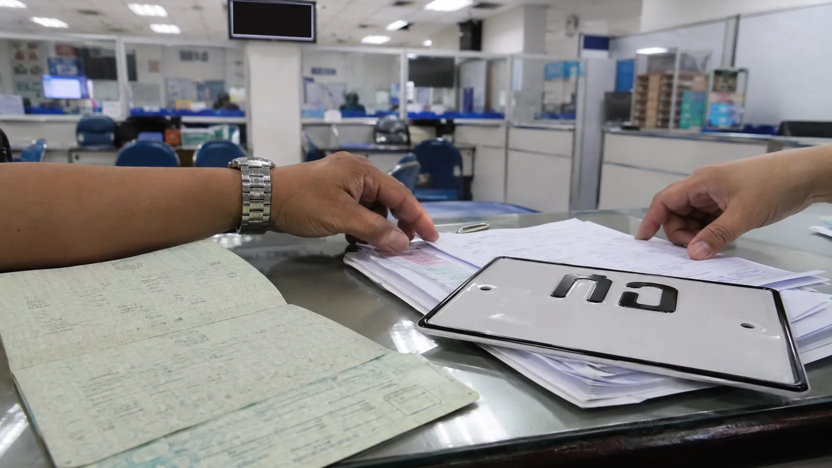 A motorcycle registration book (the green book) and a new plate on a Land Transport Department counter.